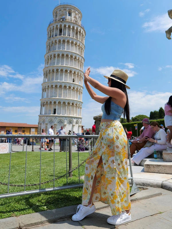 Woman with a silk flower skirt and blue denim bustier visiting the leaning Tower of Pisa in Italy.

