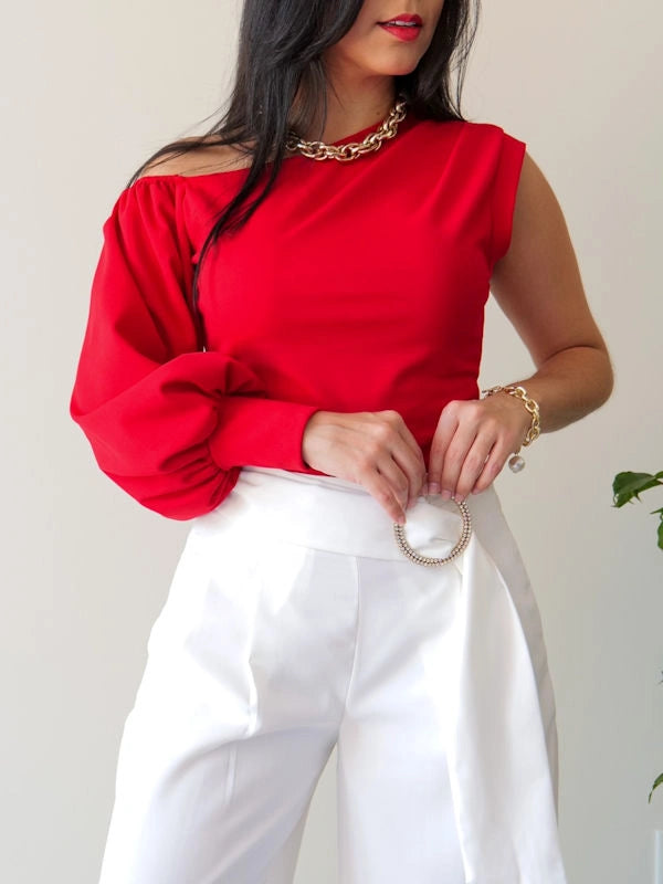 A woman wearing a one shoulder puff sleeve top and white pants. 