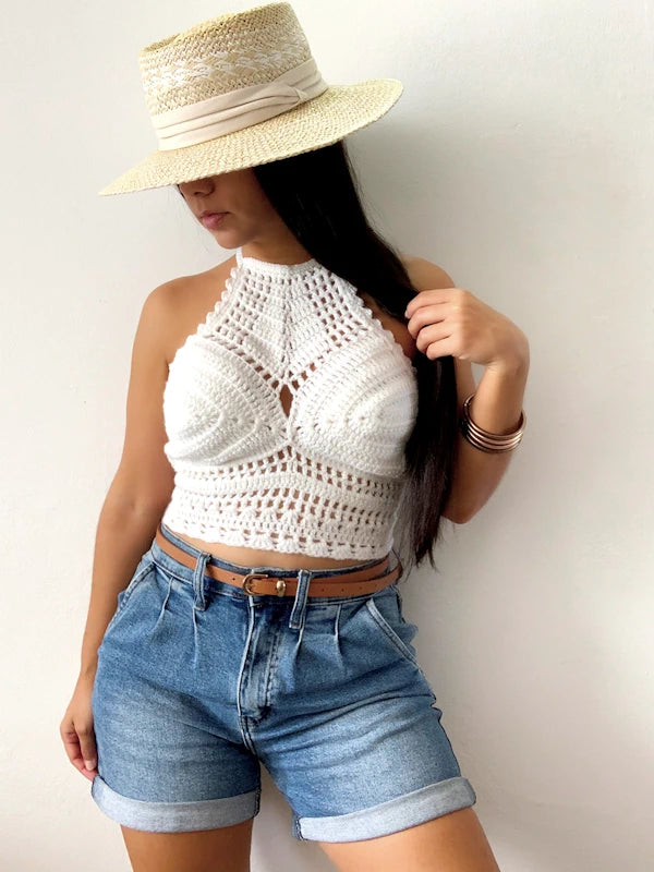 Woman wearing cuffed jean shorts in blue and a crochet white crop top. 