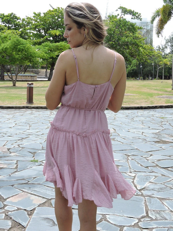 Back view of a woman in a dusty rose tiered short dress, showing the asymmetrical hem and the flow of the skirt. The thin spaghetti straps are visible at the back.