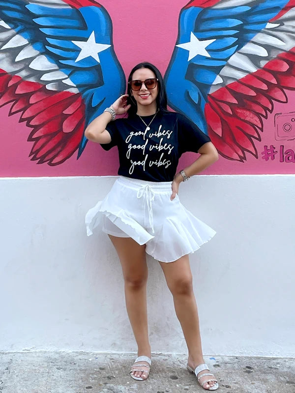A woman wearing white flowy shorts and a black t-shirt. 