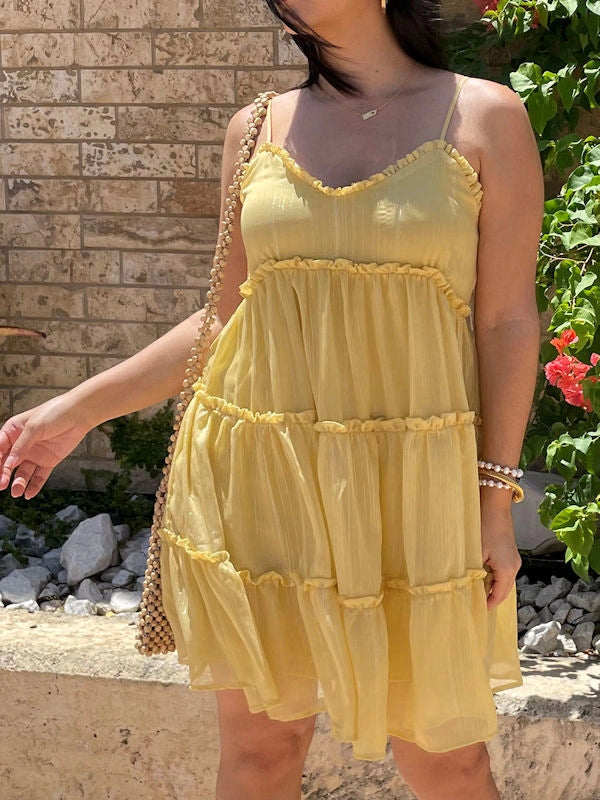 Close-up of a woman wearing a flowy tiered yellow dress, showing the V-neckline and the sheer fabric with metallic details.