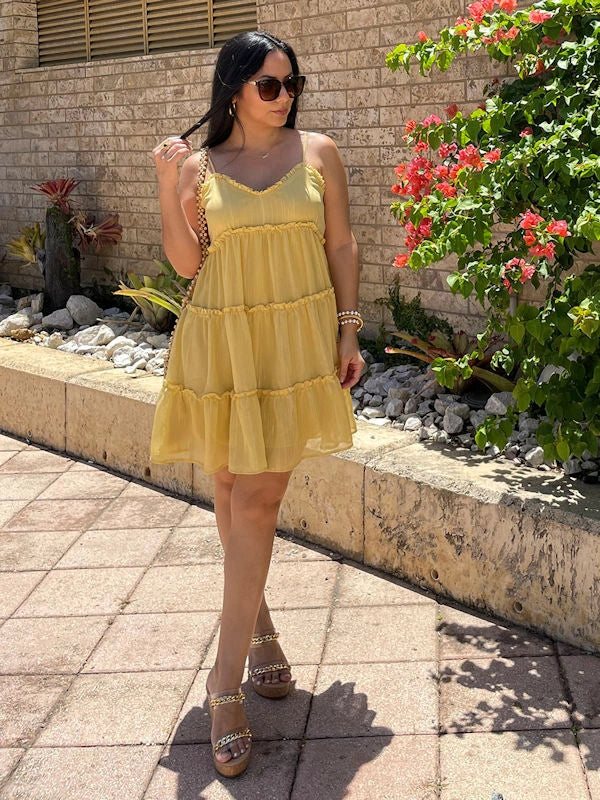 Woman in a yellow flowy sundress with a tiered skirt, posing outdoors with sunglasses and bracelets.