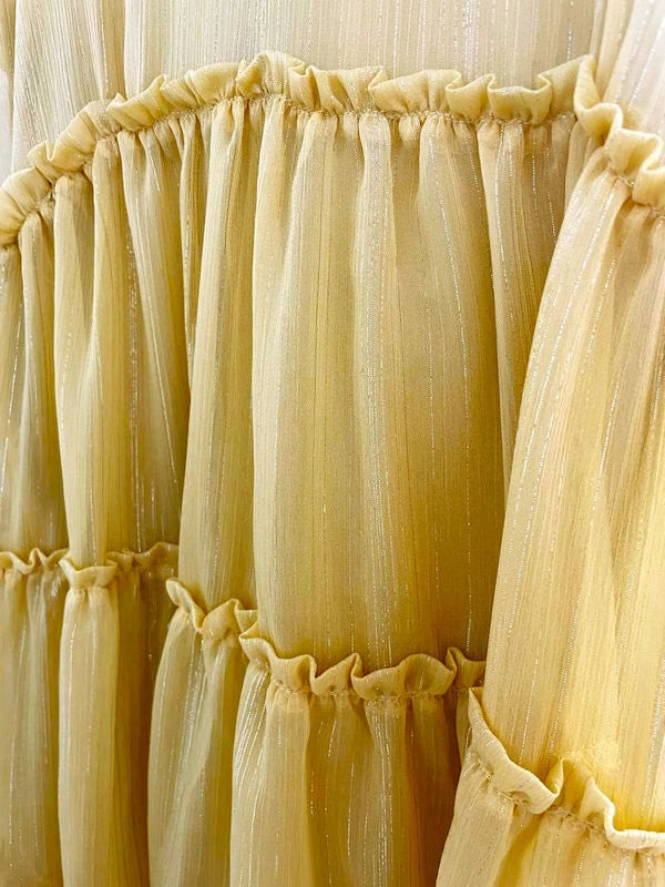 Close-up detail of the sheer yellow fabric and ruffled tiers of a lightweight summer dress with subtle metallic pinstripes.